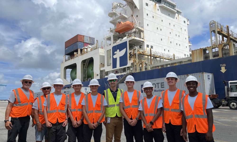 Group of workers in safety vests and helmets in front of a large ship.